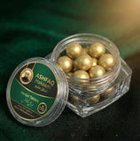 ASHFAQ Hakeem herbal tablets in a clear jar with gold-coated balls on a green background